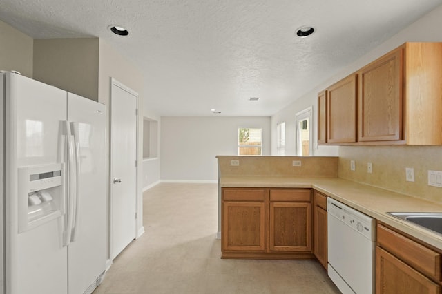 kitchen featuring brown cabinetry, a textured ceiling, light countertops, a peninsula, and white appliances