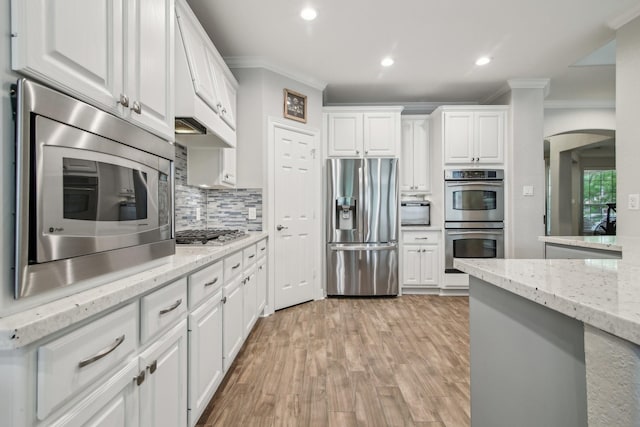 kitchen featuring crown molding, white cabinetry, arched walkways, backsplash, and stainless steel appliances
