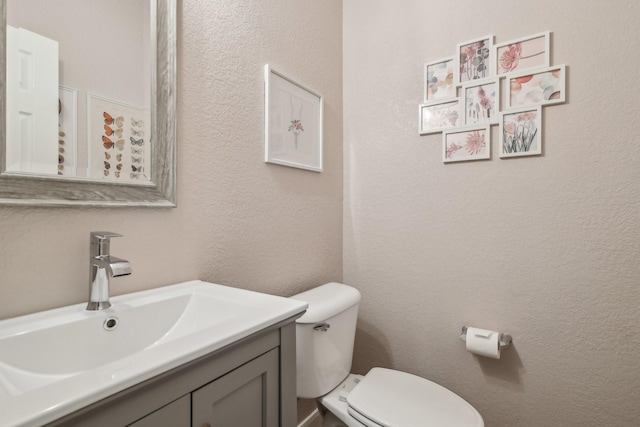 half bath featuring vanity, a textured wall, and toilet