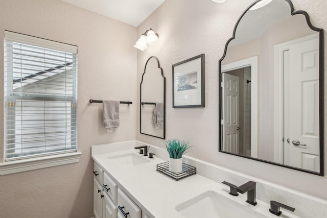 full bath with double vanity, a sink, and a textured wall