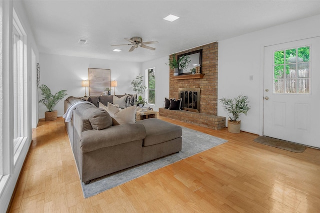 living area with a ceiling fan, visible vents, a brick fireplace, baseboards, and light wood-style flooring