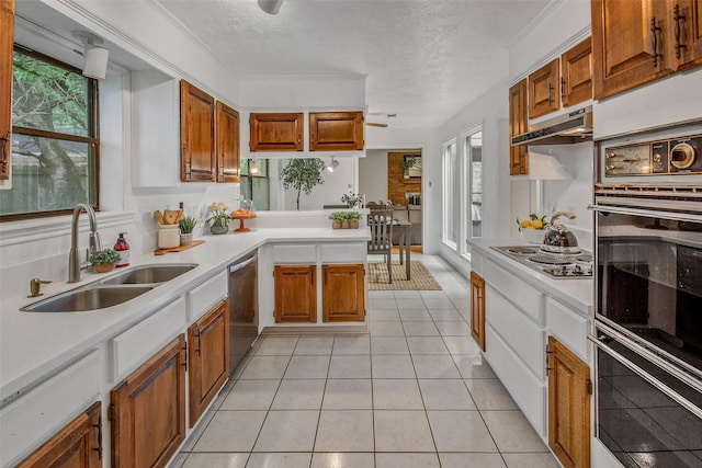 kitchen featuring a textured ceiling, appliances with stainless steel finishes, brown cabinets, a sink, and light countertops