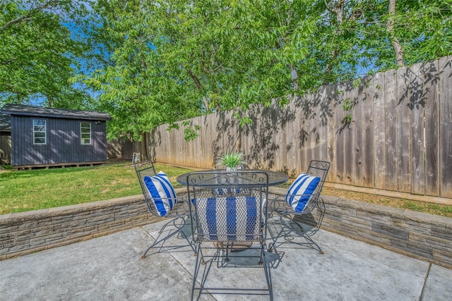 view of patio / terrace with a fenced backyard, a storage unit, outdoor dining space, and an outdoor structure