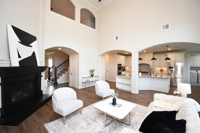19019 Kimber Creek Ln, Cypress, TX 77429 - living room with washer and clothes dryer, a towering ceiling, a glass covered fireplace, dark wood-type flooring, and stairway