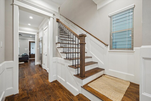 stairway with crown molding, a wainscoted wall, wood finished floors, and a decorative wall
