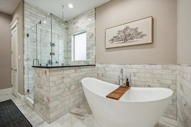 bathroom featuring marble finish floor, a stall shower, a soaking tub, and tile walls