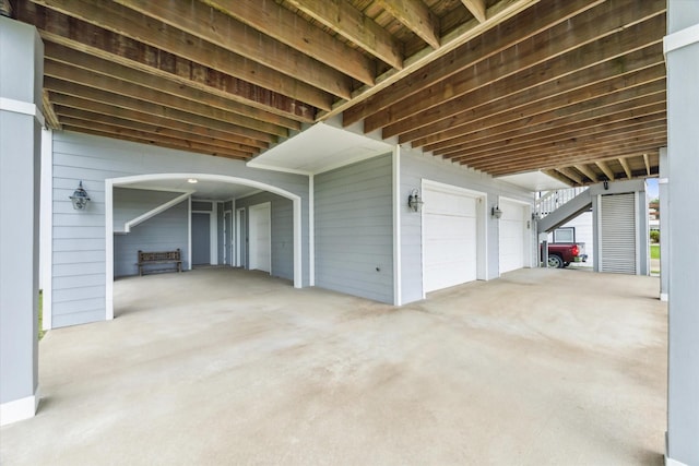 exterior space with carpet floors, a garage, arched walkways, and wooden walls