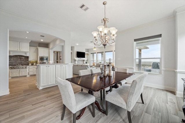 dining room with visible vents, crown molding, arched walkways, light wood-type flooring, and an inviting chandelier