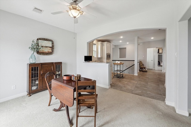 dining space with ceiling fan, light colored carpet, arched walkways, baseboards, and visible vents