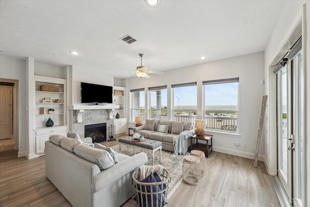 living area with a ceiling fan, visible vents, a fireplace, light wood-type flooring, and baseboards