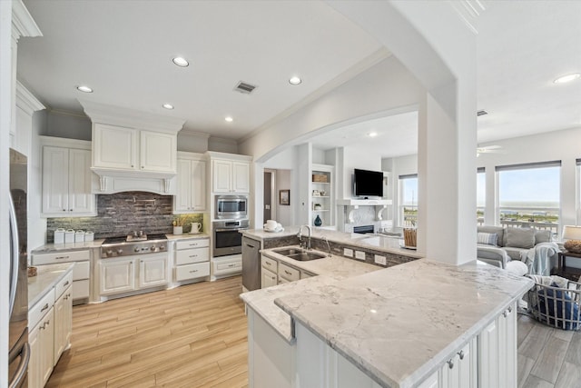 kitchen with a fireplace, open floor plan, arched walkways, a sink, and appliances with stainless steel finishes