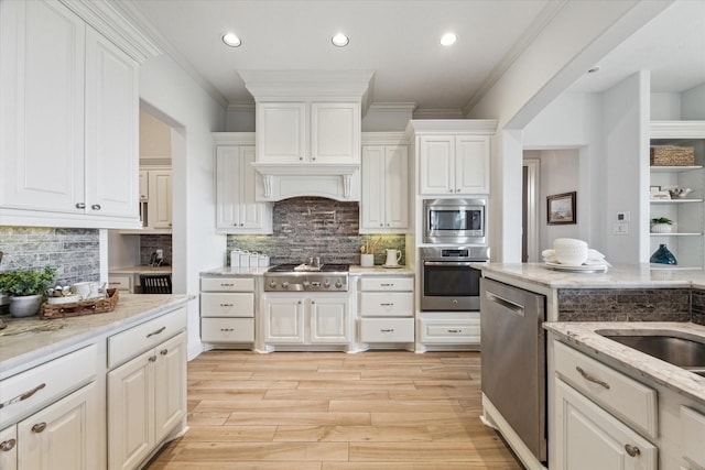 kitchen featuring appliances with stainless steel finishes, light stone counters, light wood-style flooring, white cabinetry, and ornamental molding