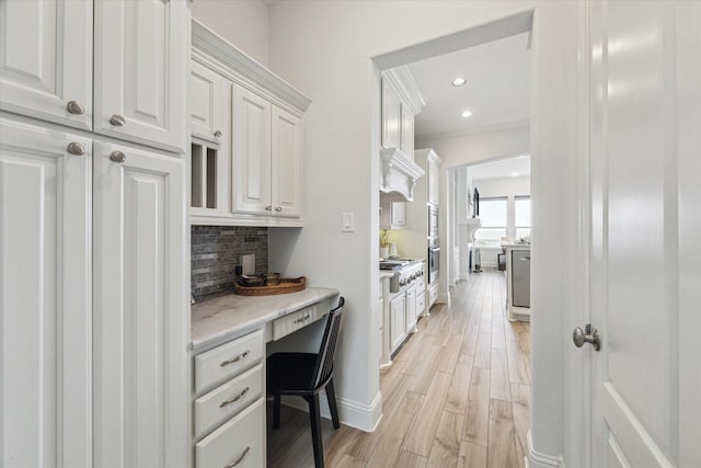 interior space with crown molding, built in desk, baseboards, light wood-style floors, and recessed lighting