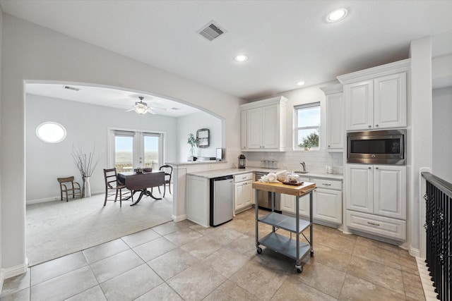 kitchen featuring light countertops, arched walkways, stainless steel microwave, and white cabinetry