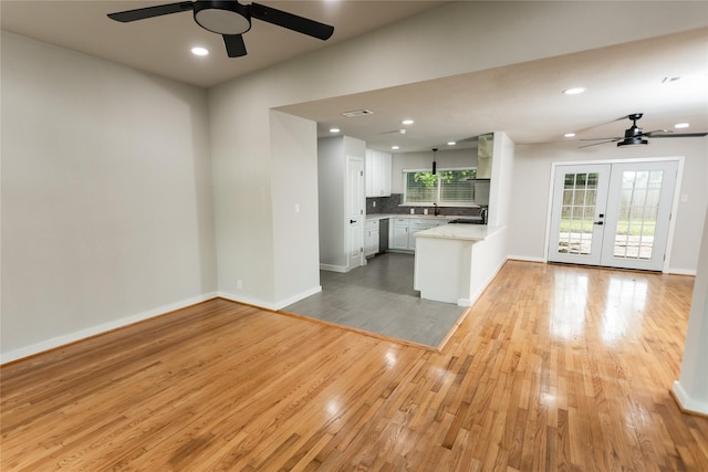 unfurnished living room with a ceiling fan, baseboards, french doors, and light wood-type flooring