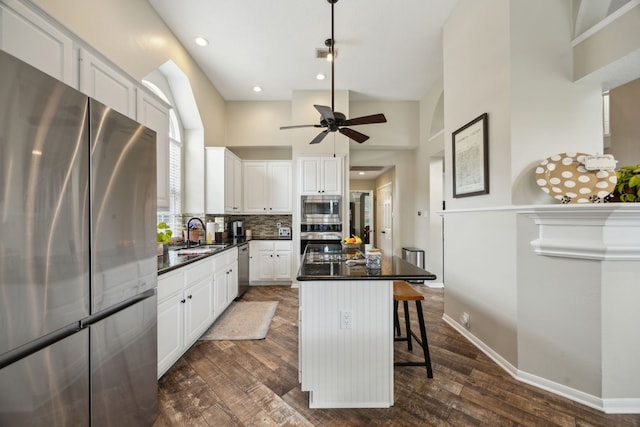 kitchen featuring dark countertops, dark wood-type flooring, white cabinetry, a sink, and appliances with stainless steel finishes