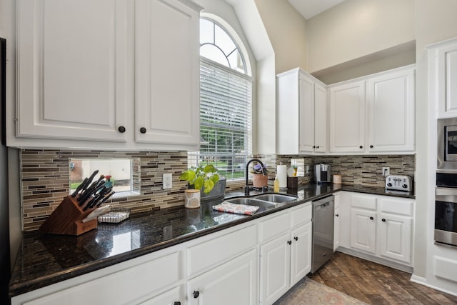 kitchen featuring appliances with stainless steel finishes, tasteful backsplash, a sink, white cabinets, and dark stone counters