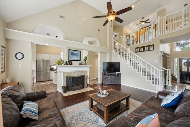 living area with ceiling fan, a fireplace, high vaulted ceiling, wood finished floors, and stairway