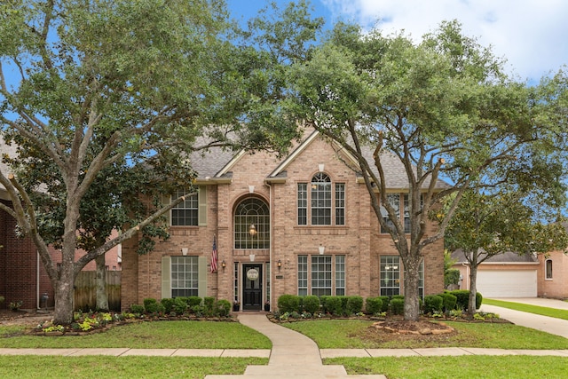 view of front of house with a front lawn, fence, brick siding, a shingled roof, and driveway