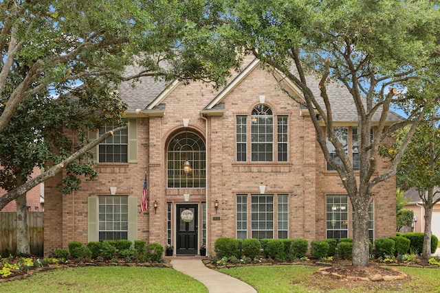 view of front of home with fence, a shingled roof, a front yard, and brick siding