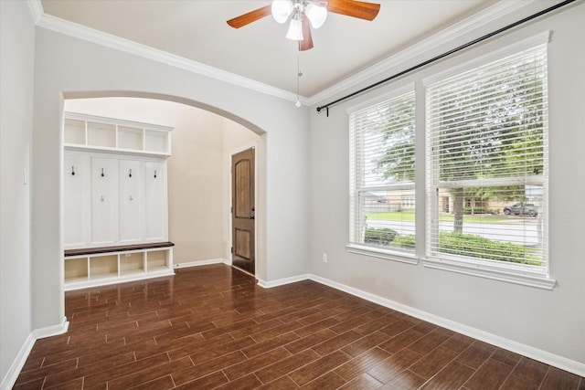 unfurnished room featuring a ceiling fan, arched walkways, dark wood finished floors, baseboards, and ornamental molding