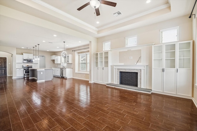 unfurnished living room featuring a raised ceiling, a fireplace with raised hearth, a ceiling fan, recessed lighting, and visible vents