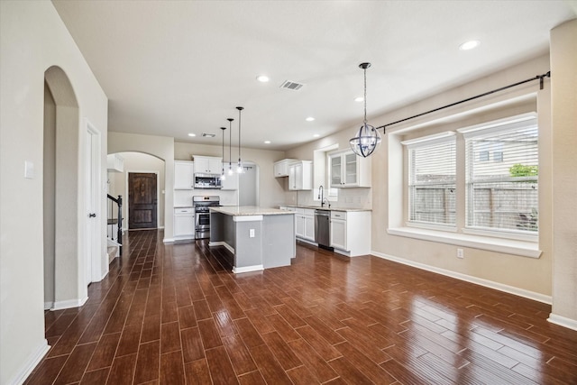 kitchen featuring arched walkways, a center island, stainless steel appliances, baseboards, and visible vents