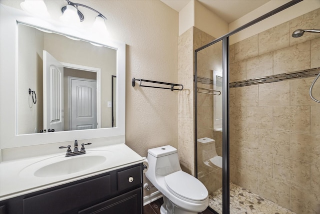full bath featuring vanity, toilet, a textured wall, and a stall shower
