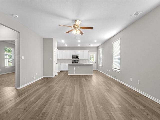 unfurnished living room featuring visible vents, a ceiling fan, baseboards, and a wealth of natural light