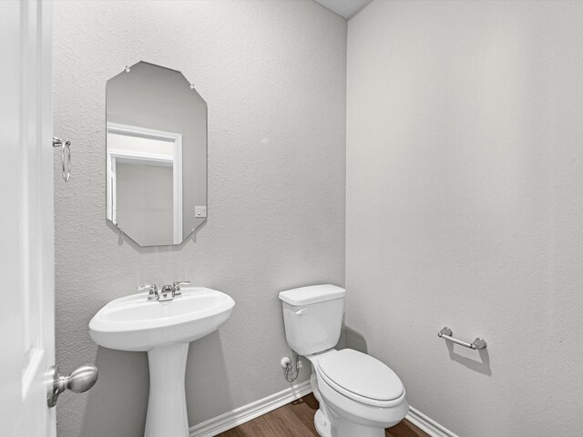 half bath featuring baseboards, a sink, wood finished floors, and toilet