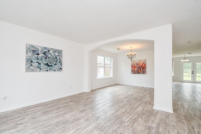 empty room with arched walkways, baseboards, light wood-style flooring, and a chandelier