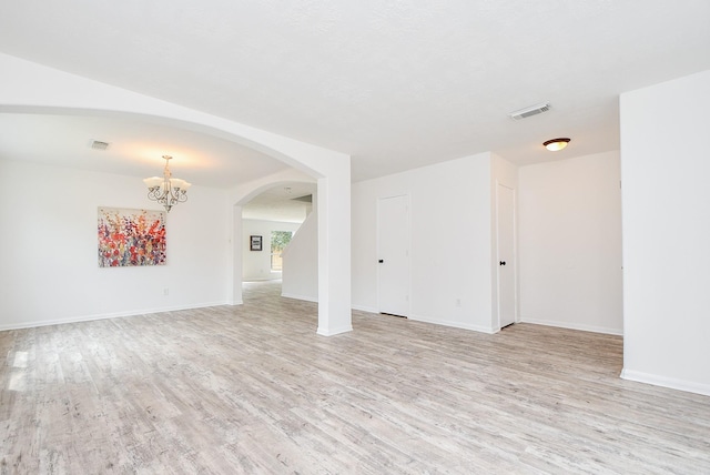 spare room with a chandelier, arched walkways, visible vents, and light wood-type flooring