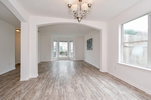 unfurnished room with arched walkways, baseboards, wood finished floors, and a chandelier