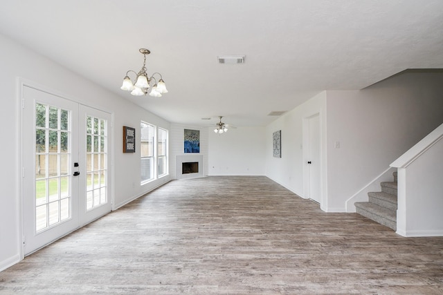 unfurnished living room with a fireplace, french doors, wood finished floors, visible vents, and stairway