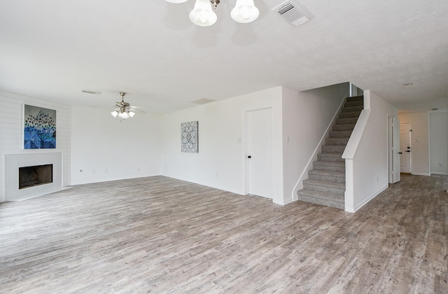 unfurnished living room featuring visible vents, baseboards, wood finished floors, and stairway