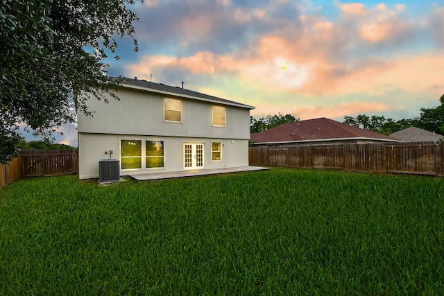 rear view of property featuring french doors, a fenced backyard, a yard, and central AC