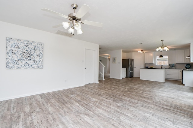 unfurnished living room featuring visible vents, light wood-type flooring, baseboards, ceiling fan with notable chandelier, and stairs