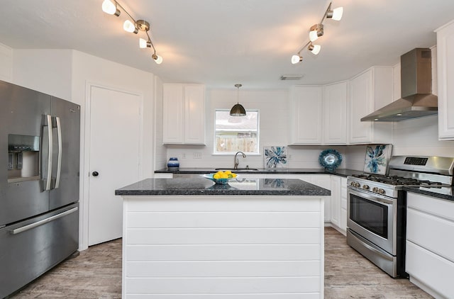 kitchen with wall chimney range hood, track lighting, white cabinets, light wood finished floors, and stainless steel appliances