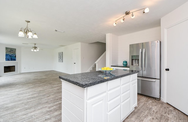 kitchen featuring a kitchen island, a large fireplace, light wood-type flooring, white cabinets, and stainless steel fridge