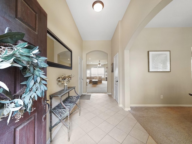 foyer entrance featuring light tile patterned floors, arched walkways, baseboards, and light colored carpet