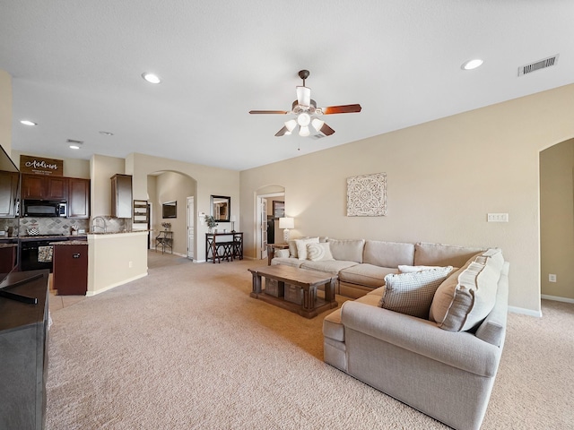 living room featuring ceiling fan, light colored carpet, visible vents, arched walkways, and baseboards