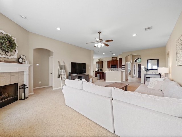 living area featuring ceiling fan, arched walkways, a fireplace, light carpet, and recessed lighting