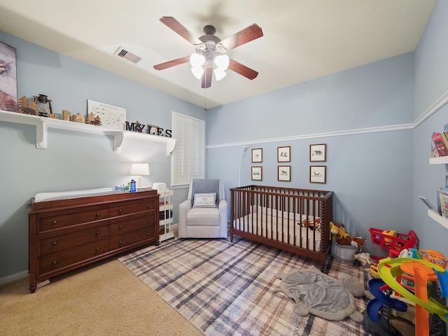 bedroom with light colored carpet, ceiling fan, visible vents, and a crib