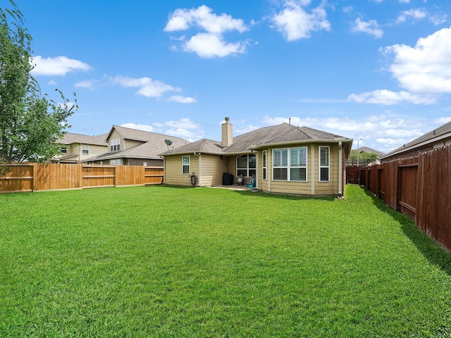 rear view of property with a lawn, a chimney, and a fenced backyard