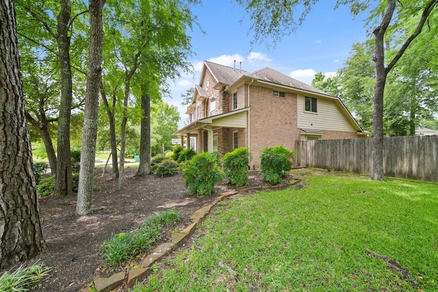 view of side of home featuring a yard, brick siding, and fence