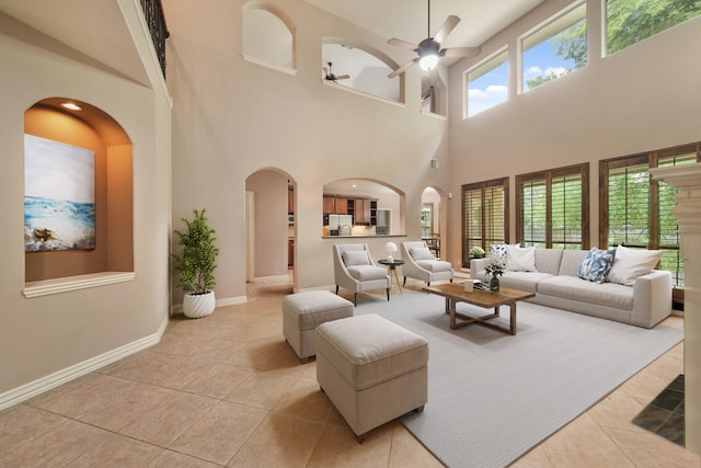 tiled living area with arched walkways, baseboards, a ceiling fan, and a towering ceiling