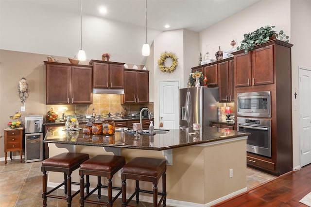 kitchen with decorative backsplash, appliances with stainless steel finishes, a sink, under cabinet range hood, and an island with sink