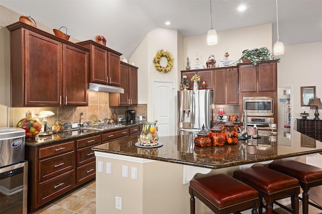kitchen with lofted ceiling, a kitchen bar, under cabinet range hood, tasteful backsplash, and appliances with stainless steel finishes