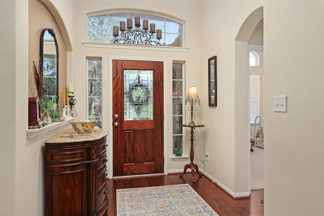 entryway featuring a towering ceiling, arched walkways, baseboards, dark wood-style floors, and a textured wall