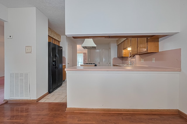 kitchen featuring brown cabinetry, visible vents, light wood finished floors, a peninsula, and black refrigerator with ice dispenser